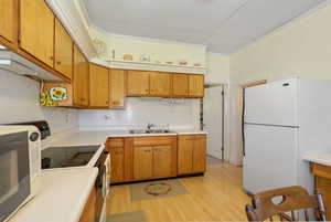Kitchen featuring white appliances, light countertops, light wood-type flooring, brown cabinetry, and ornamental molding