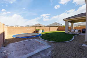 Fenced backyard featuring a trampoline and a patio area