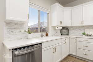 Kitchen featuring stainless steel dishwasher, white cabinets, tasteful backsplash, light wood-style floors, and light stone countertops