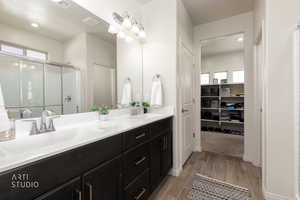 Full bath featuring a stall shower, a spacious closet, light wood finished floors, double vanity, and recessed lighting