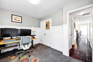 Bedroom area with a textured ceiling, dark colored carpet, wainscoting, and a decorative wall
