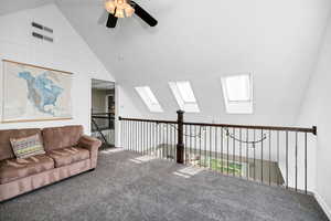 Loft area featuring high vaulted ceiling, carpet floors, a ceiling fan, a skylight, and healthy amount of natural light