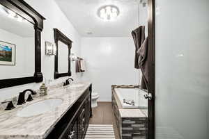 Master Bathroom with double vanity, a textured ceiling, a shower stall, and tiled tub