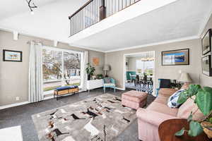 Carpeted living room with a high ceiling, a chandelier, and crown molding