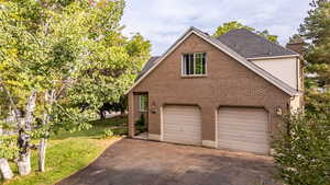 View of property exterior with driveway, brick siding, a lawn, a chimney, and a shingled roof