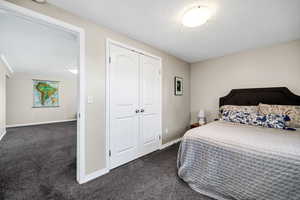 Bedroom with dark carpet, a closet, and a textured ceiling
