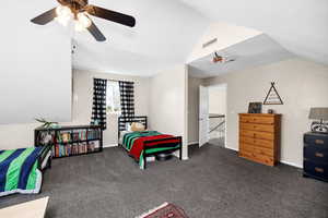 Carpeted bedroom featuring vaulted ceiling and ceiling fan