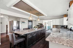 Kitchen featuring a kitchen breakfast bar, white cabinets, light stone counters, decorative light fixtures, and dark wood-style flooring