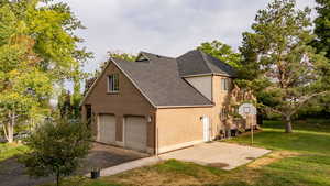 View of side of home featuring brick siding, a lawn, a garage, a shingled roof, and driveway