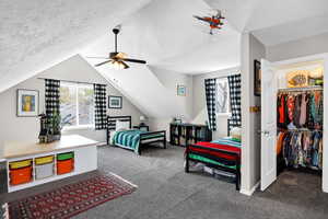Bedroom featuring dark carpet, a textured ceiling, lofted ceiling, a spacious closet, and a ceiling fan