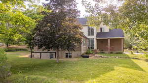 Rear view of house with a yard, brick siding, and roof with shingles