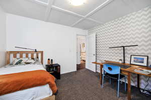 Bedroom with dark colored carpet, coffered ceiling, and wallpapered walls