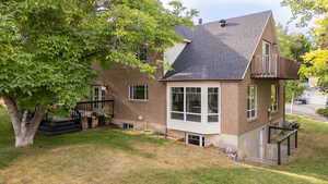 Rear view of property with a shingled roof, a yard, a balcony, brick siding, and a deck