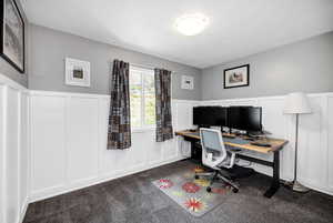 Bedroom  featuring a decorative wall, a wainscoted wall, a textured ceiling, and dark colored carpet