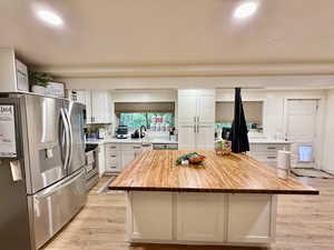 Kitchen with wooden counters, appliances with stainless steel finishes, light wood-style flooring, white cabinetry, and a center island