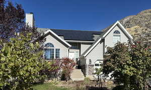 View of front of home with roof mounted solar panels, a chimney, and a shingled roof