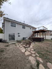 Back of property with a hot tub, a patio, stairway, and a wooden deck