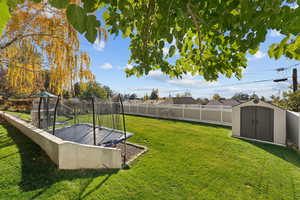 Fenced backyard featuring a trampoline and a shed