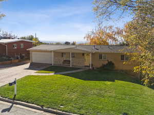 Ranch-style home with a front yard, concrete driveway, covered porch, and a garage