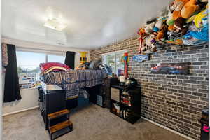 Bedroom featuring multiple windows, carpet floors, a textured ceiling, and brick wall