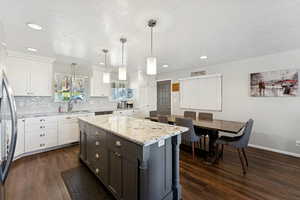 Kitchen featuring white cabinetry, light stone countertops, decorative light fixtures, dark wood-type flooring, and recessed lighting