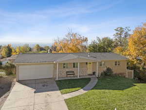 Ranch-style home featuring covered porch, a front lawn, driveway, a garage, and brick siding