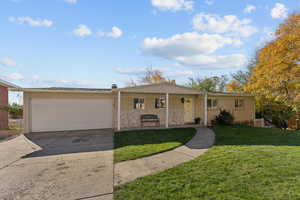 Ranch-style home featuring a porch, an attached garage, concrete driveway, a front yard, and brick siding