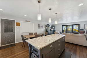 Kitchen featuring light stone counters, decorative light fixtures, dark wood-style floors, recessed lighting, and a kitchen island