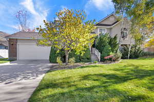 View of property hidden behind natural elements featuring brick siding, concrete driveway, an attached garage, stucco siding, and stairs