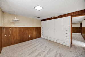 Unfurnished bedroom featuring wooden walls, a wainscoted wall, wallpapered walls, and light colored carpet