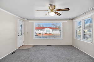 Carpeted empty room featuring a ceiling fan and ornamental molding