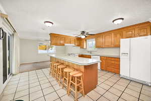 Kitchen with white appliances, light countertops, light tile patterned floors and a breakfast bar area.