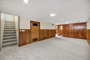 Finished below grade area with stairs, carpet floors, wooden walls, recessed lighting, and wainscoting