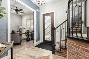 Foyer featuring a ceiling fan, light wood-style tile flooring, stairs, and a chandelier