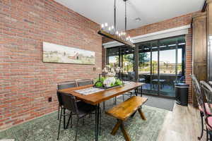 Dining space with brick wall, a chandelier, and light wood tile floors
