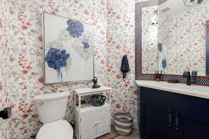 Half bathroom with vanity, wallpapered walls, and wood tile finished floors