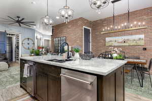 Kitchen with dark brown cabinets, stainless steel dishwasher, open floor plan, brick wall, and a barn door leading into laundry room