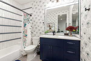 Full bathroom with wallpapered walls, vanity, shower / bath combo with shower curtain, and light tile patterned floors
