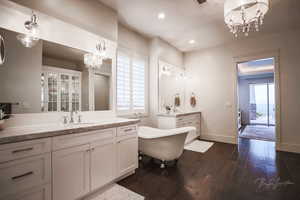 Full bath with a chandelier, two vanities, a freestanding bath, dark wood-style floors, and recessed lighting
