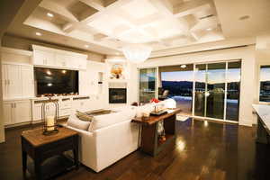 Living area with coffered ceiling, beam ceiling, dark wood-style floors, a glass covered fireplace, and recessed lighting