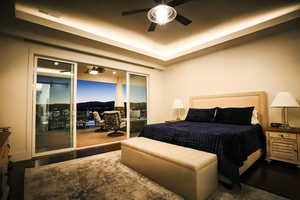 Bedroom with wood finished floors, access to exterior, a raised ceiling, a desk, and a ceiling fan