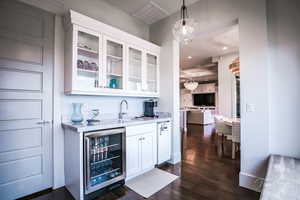 Bar featuring white cabinets, glass insert cabinets, beverage cooler, decorative light fixtures, and dark wood-style flooring