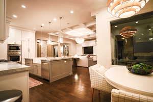 Kitchen with coffered ceiling, dark wood finished floors, recessed lighting, open floor plan, and light stone counters