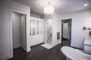 Bathroom with a walk in closet, dark wood-style flooring, a freestanding bath, a stall shower, and a chandelier