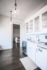 Bar area featuring white cabinets, pendant lighting, light stone counters, dark wood finished floors, and glass insert cabinets