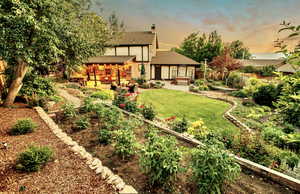 Back of house at dusk featuring a fenced backyard, a patio area, roof with shingles, a chimney, and a garden