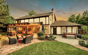 Back of house with a hot tub, a patio area, a chimney, roof with shingles, and stucco siding