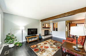 Living area with dark wood-style flooring, beam ceiling, and a tile fireplace