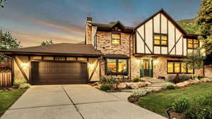English style home featuring a chimney, an attached garage, concrete driveway, stucco siding, and roof with shingles