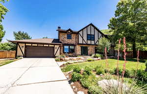 Tudor home with brick siding, a chimney, an attached garage, concrete driveway, and stucco siding
